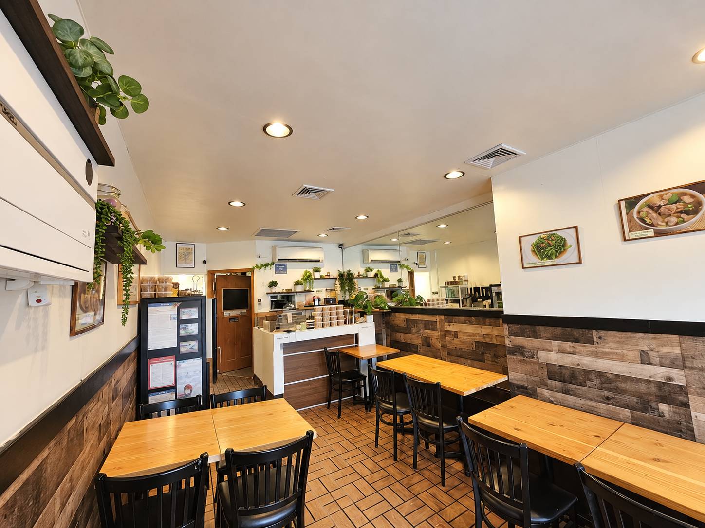 Dining room with wood-panel walls, wood tables, black chairs, hanging plants, a mirror wall and the counter at the back.